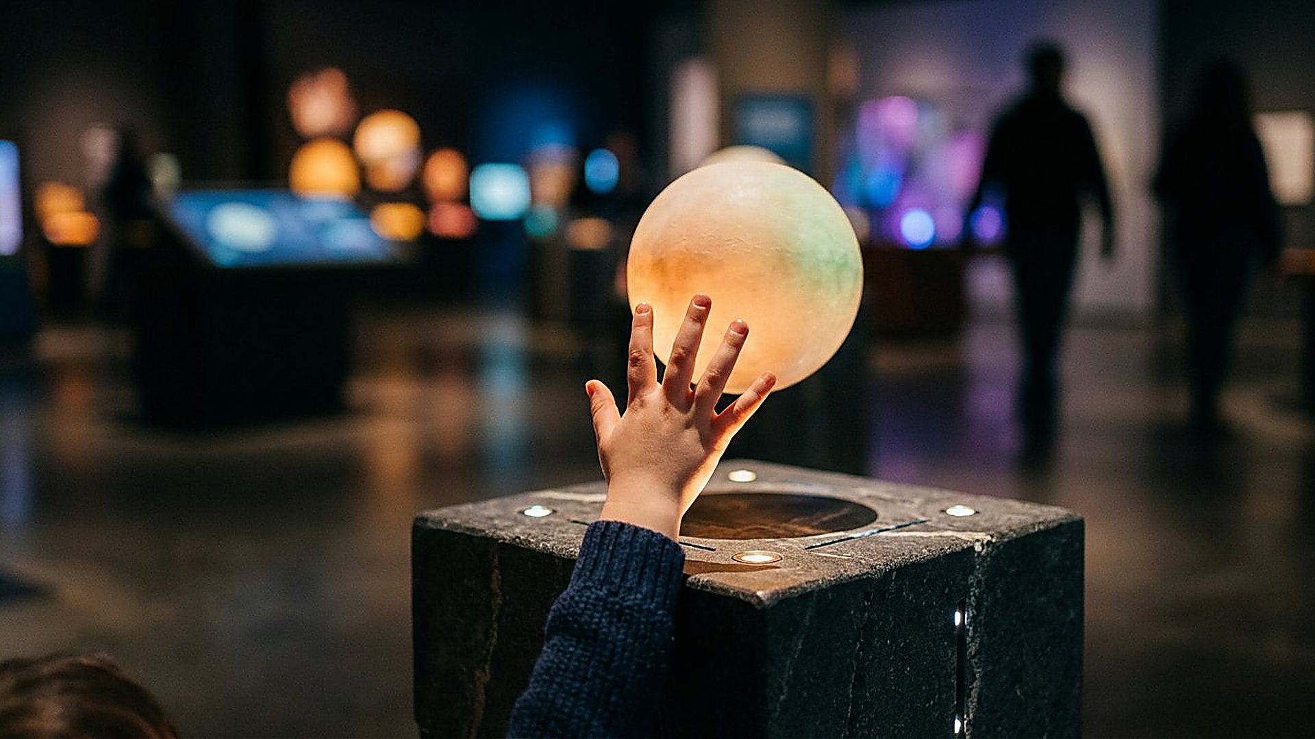 Main d'enfant touchant une sphère lumineuse sur un socle interactif